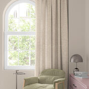 Janela com cortina florida colorida em vermelho, laranja e azul, poltrona verde e pequena mesa com abajur